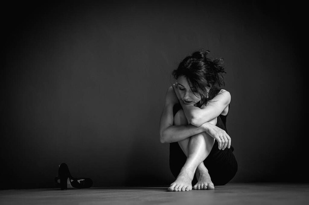 Black and white classic photo, young pretty girl sitting on the floor, pensive, thinking, depression, dark background, low key - Foto, imagen