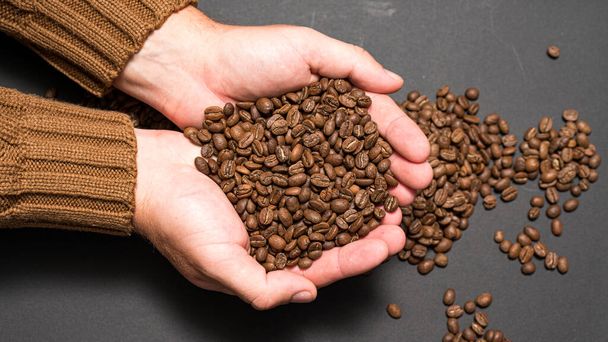 Male hands hold coffee on a dark background, coffee beans in hands. - Photo, Image