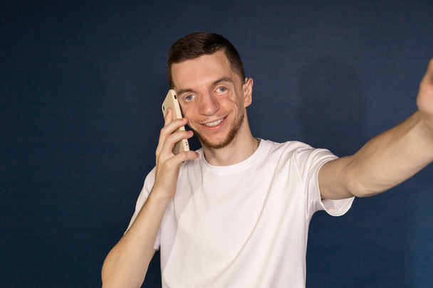 Hombre de camiseta blanca con síndrome de Treacher se toma selfies hablando por teléfono. - Foto, Imagen