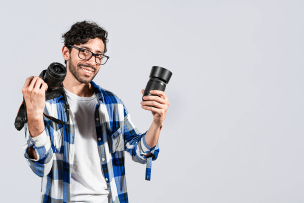 Portrait of smiling photographer man showing a camera and lens on isolated background. Smiling young man holding a camera isolated, Smiling photographer guy showing a camera and lens - Photo, Image