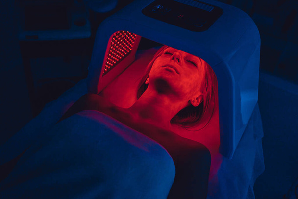 LED red light is treating the facial skin of a young woman. High quality 4k footage - Foto, Imagen