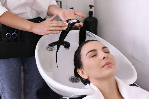 Professional hairdresser applying conditioner on woman's hair in beauty salon, closeup - Photo, image