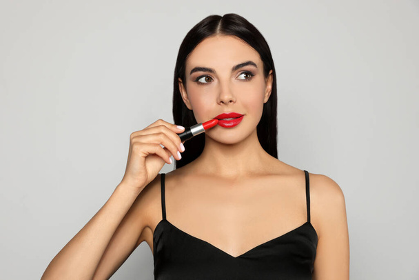 Young woman applying red lipstick on light gray background - Foto, afbeelding