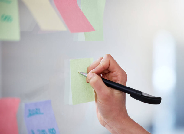 Closeup of unknown business woman writing on sticky notes on a transparent board to brainstorm in an office. Caucasian professional sticking a note on visual aid while planning a strategy with ideas. - Photo, Image