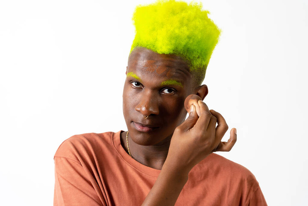 An androgynous black man posing putting on makeup, LGTBI concept, applying blusher, white background - Photo, Image