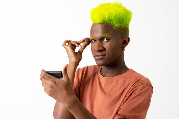 An androgynous black man posing putting on makeup, LGTBI concept, portrait applying blusher - Foto, Bild