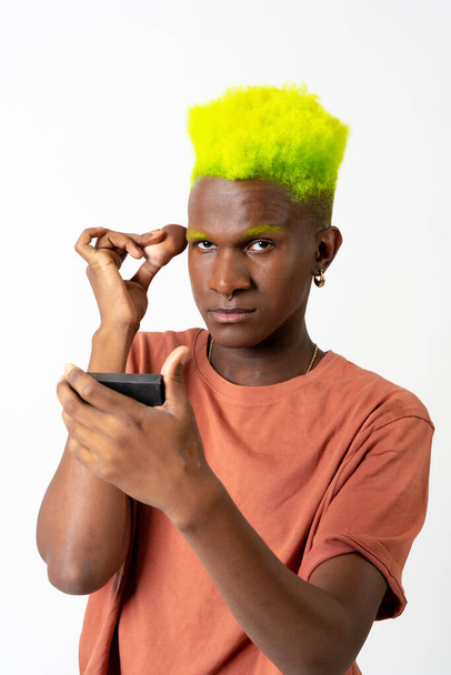 An androgynous black man posing putting on makeup, LGTBI concept, portrait applying blusher - Φωτογραφία, εικόνα