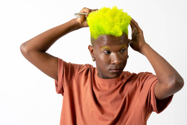 Gay black ethnic man putting on makeup, LGTBI concept, combing his gorgeous green hair - Photo, Image