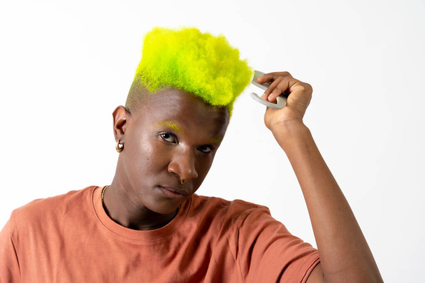 Гей черный этнический мужчина наносит макияж, LGTBI концепции, расчесывая зеленый современный прическу - Фото, изображение