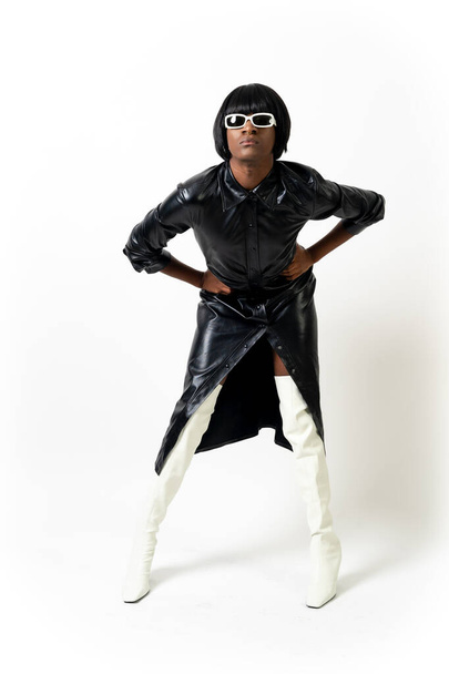 Black ethnic man in studio with white background, LGTBI concept, wearing leather skirt and white heels - Fotó, kép