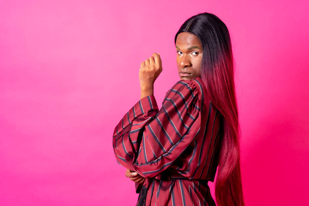 Black ethnic man in a studio, LGTBI concept, wearing a red kimono and a long wig - Foto, afbeelding