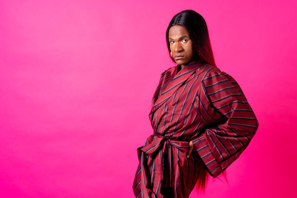 Black ethnic man in a studio, LGTBI concept, with a wig on a pink background - Foto, Imagem