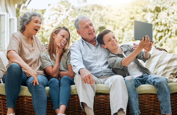 Die Kinder machen gerne Selfies. ein kleiner Junge, der ein digitales Tablet benutzt, während er zu Hause mit seiner Schwester und seinen Großeltern sitzt - Foto, Bild