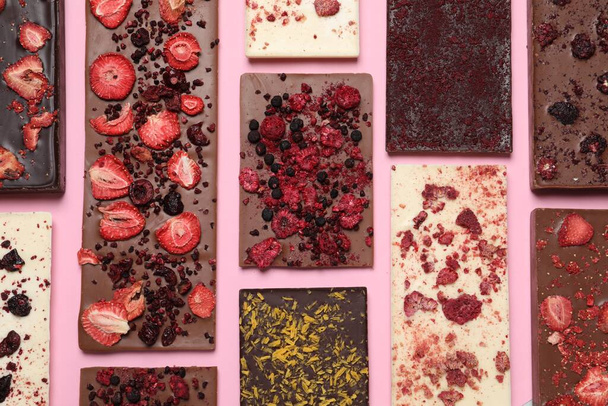 Different chocolate bars with freeze dried fruits on pink background, flat lay - 写真・画像