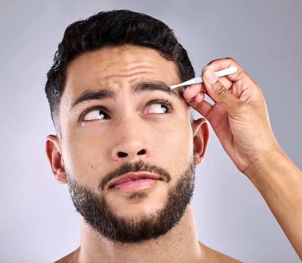Id rather just get it over with. Closeup shot of a young man plucking his eyebrows against a grey background - Foto, imagen