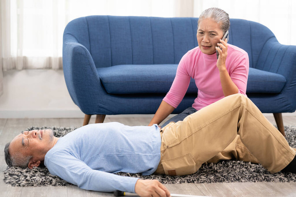 An elderly man falls unconscious in the house. An elderly woman calls for an emergency. Unconscious senior man with walking stick lying on carpet at home. selective focus - Fotografie, Obrázek