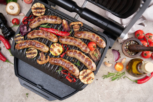 Grilled sausages and vegetables on electric grill at domestic kitchen. - Photo, Image