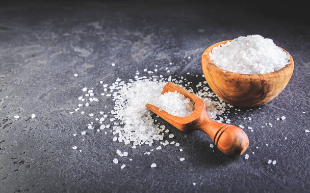 Pure natural sea salt in wooden bowl and wooden spoon on black background - Photo, Image