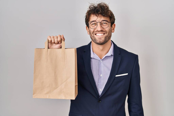 Hispanic business man holding delivery bag looking positive and happy standing and smiling with a confident smile showing teeth  - Photo, Image