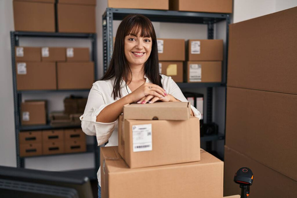 Jonge mooie Spaanse vrouw e-commerce zakenman leunend op pakketten op kantoor - Foto, afbeelding