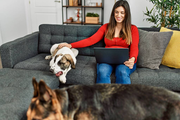 Νεαρή γυναίκα που χρησιμοποιεί φορητό υπολογιστή κάθεται στον καναπέ με το σκυλί στο σπίτι - Φωτογραφία, εικόνα