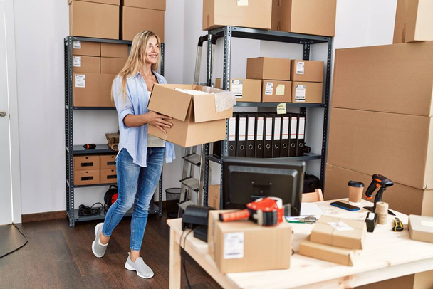 Young blonde woman ecommerce business worker holding package at office - Foto, imagen