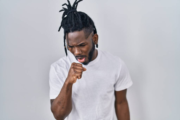 Homem africano com dreadlocks vestindo camiseta casual sobre fundo branco sentindo-se mal e tosse como sintoma de frio ou bronquite. conceito de cuidados de saúde.  - Foto, Imagem