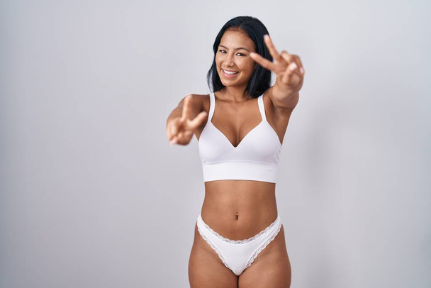 Hispanic woman wearing lingerie smiling with tongue out showing fingers of both hands doing victory sign. number two.  - Photo, Image