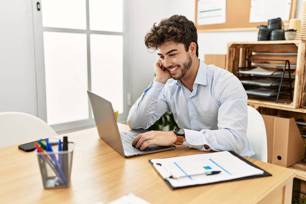 Mladý hispánský podnikatel se šťastně usmívá, když pracuje v kanceláři. - Fotografie, Obrázek