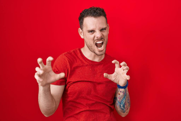 Young hispanic man standing over red background smiling funny doing claw gesture as cat, aggressive and sexy expression  - Zdjęcie, obraz