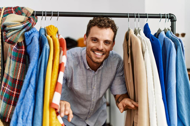 Молодий іспаномовний клієнт, посміхаючись щасливий, з'являється через одяг в магазині одягу
. - Фото, зображення