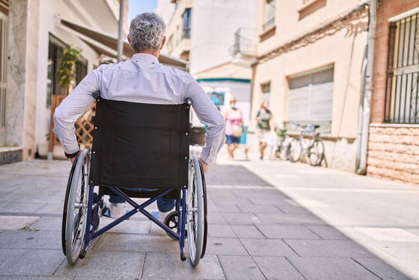 Homem hispânico de meia idade vestindo roupas de negócios sentado em cadeira de rodas na rua - Foto, Imagem