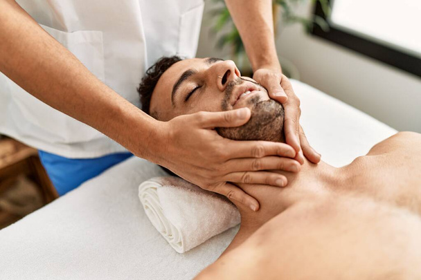 Двоє іспаномовних чоловіків терапевт і пацієнт мають масаж обличчя в центрі краси
 - Фото, зображення
