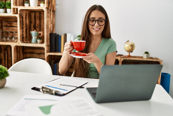 Fiatal spanyol nő laptoppal kávézik otthon az asztalon. - Fotó, kép