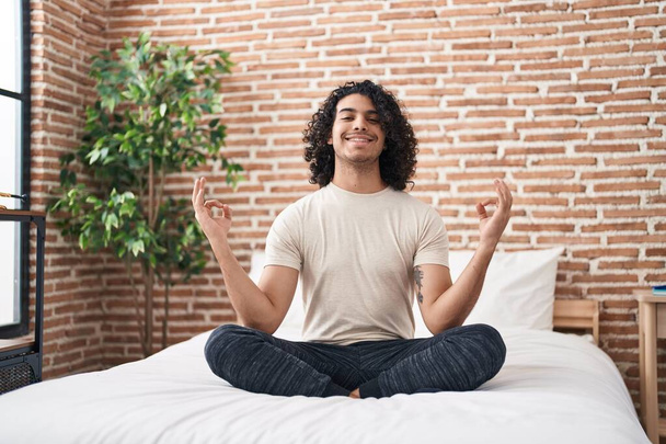 Jovem latino fazendo exercício de ioga sentado na cama no quarto - Foto, Imagem