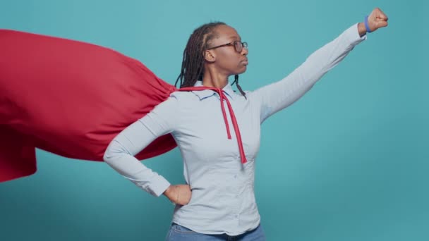 Africký americký superhrdina létající s červeným pláštěm a kostýmem přes modré pozadí. Nošení plášť s kostýmem hrdiny, aby se vydával za akční kreslený postava, ukazuje vítězství a odvahu. - Záběry, video