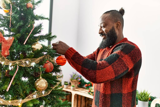 Mladý africký Američan muž usměvavý sebevědomý zdobení vánoční stromeček doma - Fotografie, Obrázek