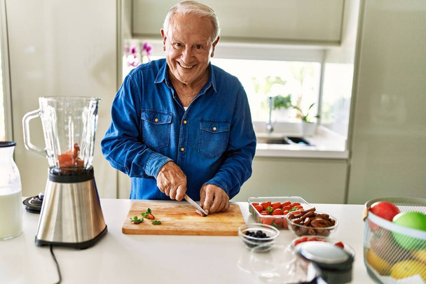 Idősebb férfi mosolygós magabiztos vágás datil a konyhában - Fotó, kép
