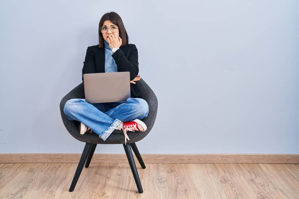 Jonge Latijns-Amerikaanse vrouw zit op stoel met behulp van computer laptop kijken gestresst en nerveus met handen op de mond bijten nagels. angstprobleem.  - Foto, afbeelding