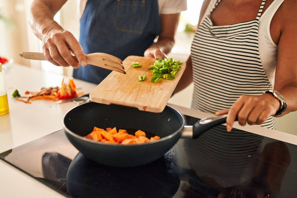 Latynoska para w średnim wieku wylewa jedzenie na patelnię w kuchni - Zdjęcie, obraz
