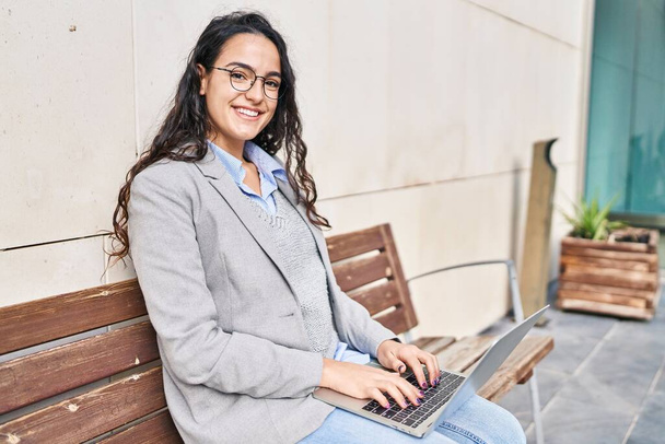 Fiatal spanyol nő végrehajtó laptoppal ül padon az utcán - Fotó, kép