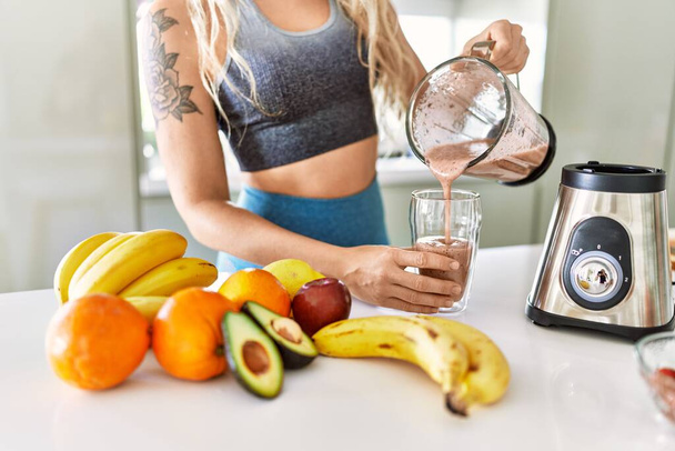 Young woman pouring smoothie on glass at kitchen - Foto, Bild