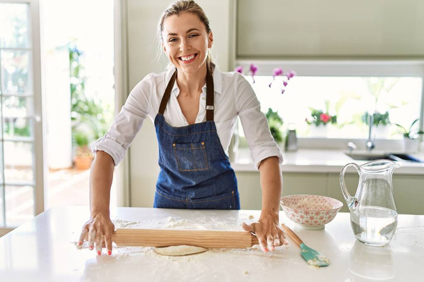 Junge blonde Frau lächelt selbstbewusst beim Kneten von Pizzateig in Küche - Foto, Bild