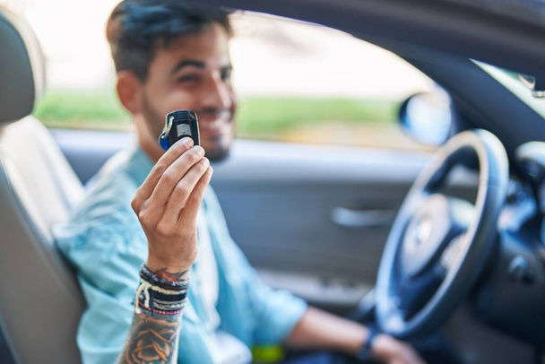 Молодий іспаномовний чоловік посміхається впевнено тримає ключ від нової машини на вулиці
 - Фото, зображення