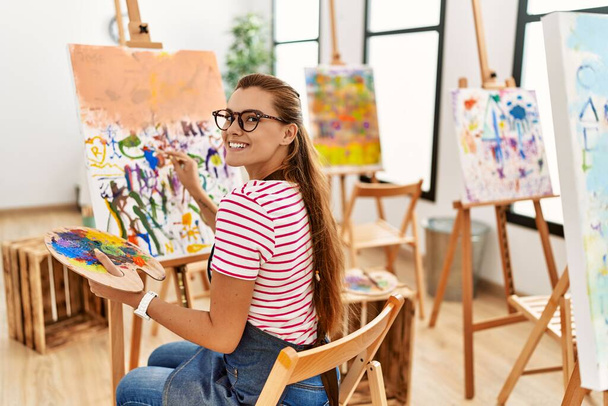Mujer joven sonriendo dibujo seguro en el estudio de arte - Foto, imagen