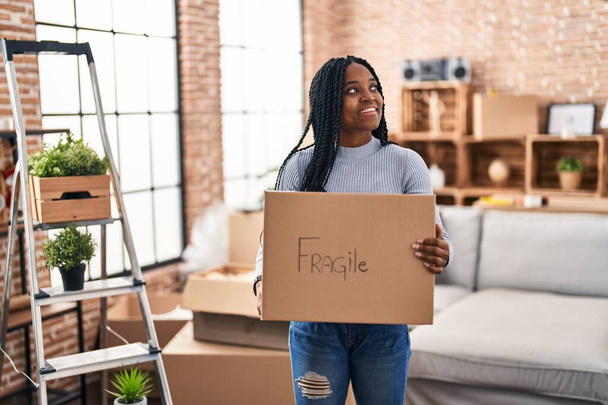 Africká americká žena se usmívá sebevědomě drží křehký balíček v novém domově - Fotografie, Obrázek