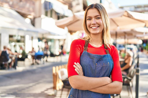 Young hispanic woman waitress standing with arms crossed gesture at coffee shop terrace - Фото, зображення