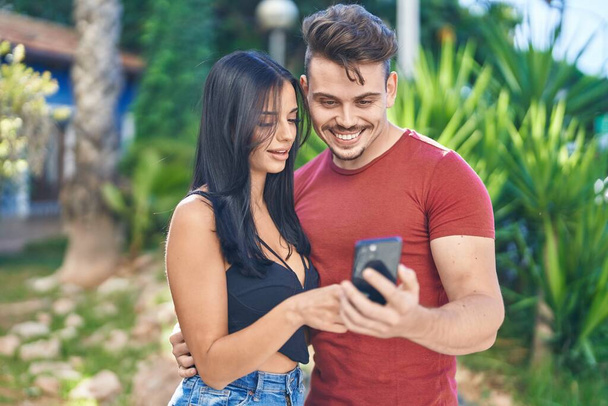 Muž a žena pár usměvavý jistý pomocí smartphone v parku - Fotografie, Obrázek
