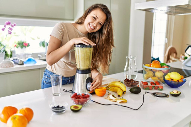 Young beautiful hispanic woman preparing vegetable smoothie with blender at the kitchen - Foto, immagini
