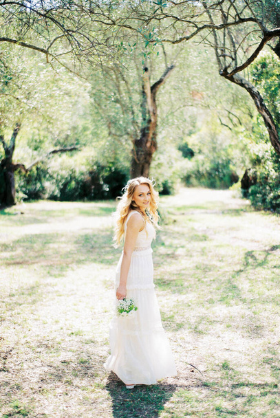 Bride with a bouquet stands with her head turned in the park. High quality photo - Foto, Bild